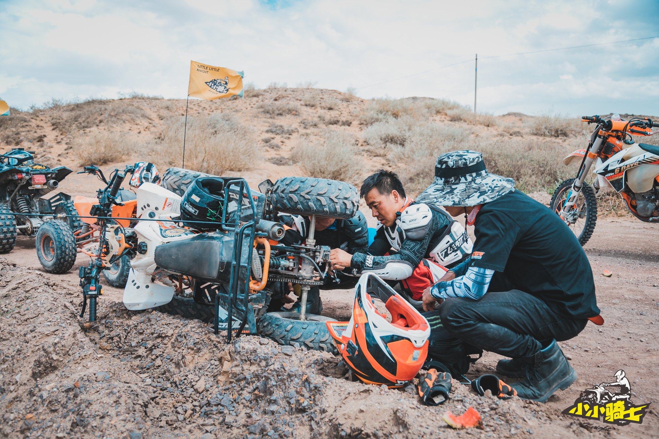 A child and coach checking rally equipment on desert terrain.